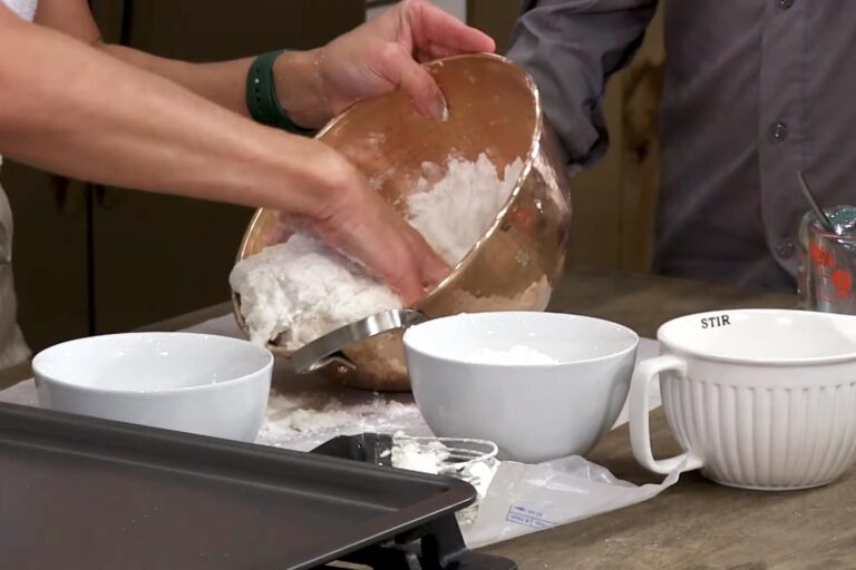 Hands mixing flour in a mixing bowl during a cooking demonstration.